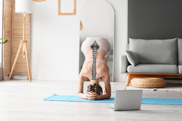 Young woman with laptop practicing yoga at home. Concept of healthy spine - obrazy, fototapety, plakaty