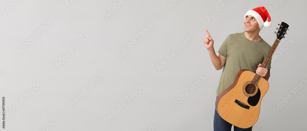 Poster Young man in Santa hat and with guitar pointing at something on grey background with space for text