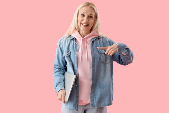 Mature female programmer with laptop pointing at something on pink background
