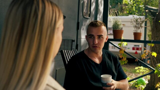 A young handsome guy and a girl are sitting on the veranda of a mobile home in camper drinking tea and talking enthusiastically