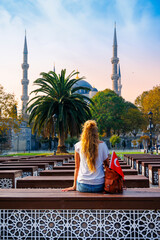 Woman tourist sitting on bench looking at the Blue mosque and palm tree, Istanbul, Turkey