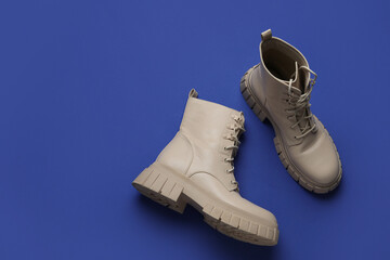 Stylish beige leather boots on blue background