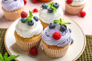 Plate of delicious cupcakes with blueberries, raspberries and mint on pink tile background