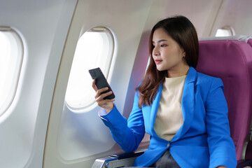 Happy Asian businesswoman uses mobile phone to check her meeting schedule during flight. Search information, take photo, check in, online chat. Technology concept, lifestyle.