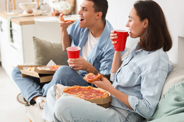 Young couple with drinks eating tasty pepperoni pizza at home