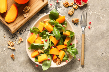 Bowl of delicious salad with persimmon, pomegranate seeds and walnut on grey background