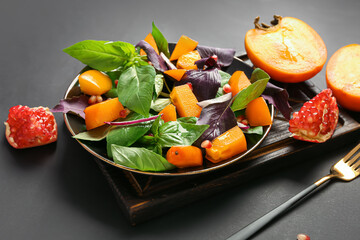 Plate of delicious salad with persimmon, pomegranate seeds and onion on black background