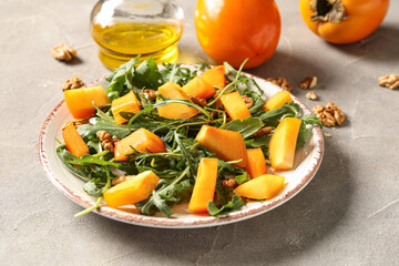 Plate of delicious salad with persimmon and walnut on grey background