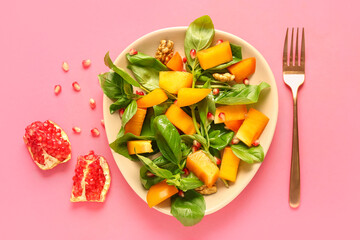Plate of delicious salad with persimmon, pomegranate seeds and walnut on pink background