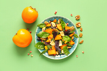 Plate of delicious salad with persimmon, pomegranate seeds and walnut on green background