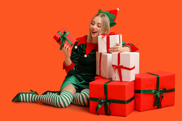 Young woman in elf costume with Christmas gift boxes on orange background