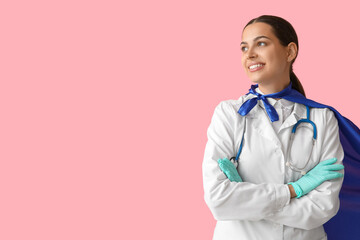 Beautiful female doctor in superhero costume on pink background