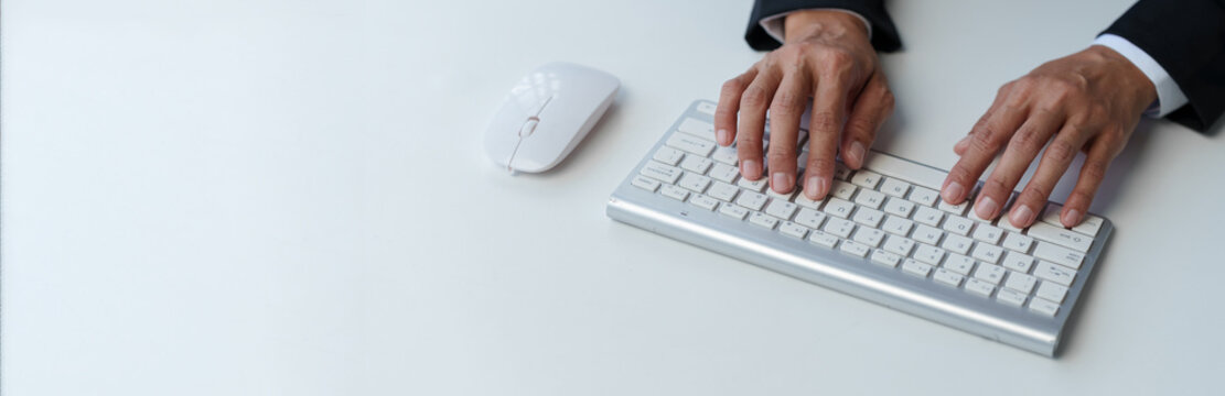 Cropped view of businessman typing on keyboard Hand typing on wireless computer keyboard and mouse in office, writing, typing email or communicating online.
