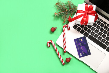 Fototapeta na wymiar Christmas gift box with laptop, candy canes and credit card on green background