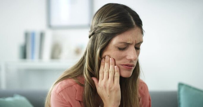 Woman, toothache and pain on living room sofa in oral, gum or mouth injury emergency at home. Face of sick female person with sore teeth, jaw or cavity and gingivitis problem on lounge couch at house