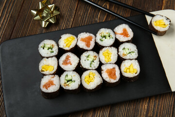 Board with tasty sushi rolls and bow on wooden background