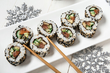 Plate with tasty sushi rolls and snowflakes on white wooden background