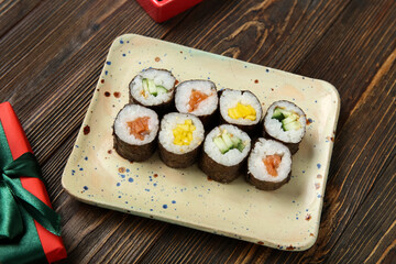 Plate with tasty sushi rolls on wooden background