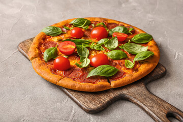 Wooden board of delicious Pepperoni pizza with tomatoes and basil on grey background