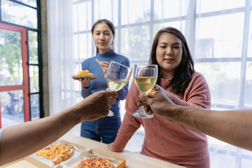 Group of happy Asian young people with friends celebrate clinking glasses during party, food, pizza, snacks with silverware Stemware glass and delicious food