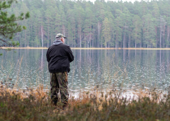 Fototapeta premium fisherman on the shore of a swamp lake, forest and swamp vegetation, rainy and cloudy day