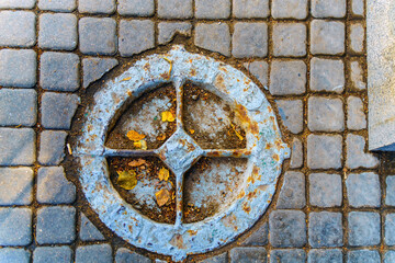 Obraz na płótnie Canvas Very old manhole on the pavement made of square stones