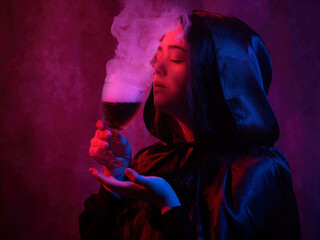 Mysterious woman holds glass with dark liquid and smoke effect.