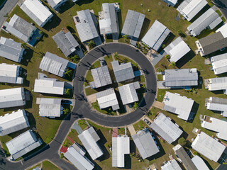 A mobile home neighborhood, configured in a circular layout, is shown from an aerial, daytime view among the community's streets.