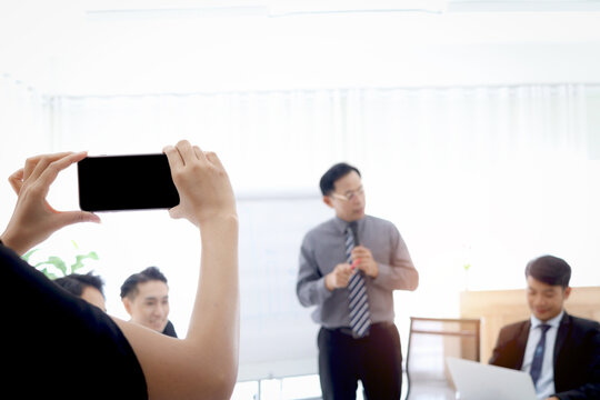 Hand holding mobile phone for taking photo or VDO of business discussing conference with blurred background of brainstorming presentation, record the memoirs of success company teamwork meeting.