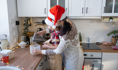 Mom and daughter in the white kitchen knead the dough in the bowl for gingerbread and cookies with...