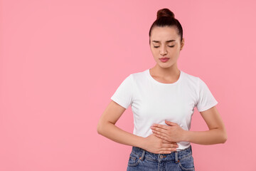 Woman suffering from abdominal pain on pink background, space for text. Unhealthy stomach