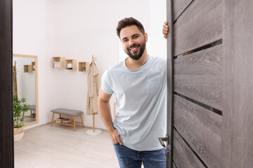Happy man standing near door, space for text. Invitation to come indoors