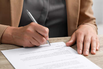 Woman signing document at wooden table indoors, closeup