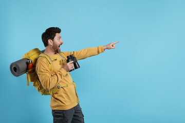 Emotional man with backpack and binoculars on light blue background, space for text. Active tourism