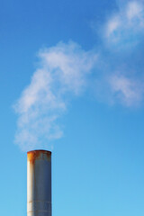 Vertical photo of a smoking chimney against the sky.