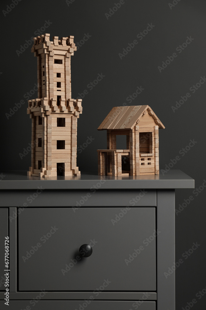 Poster Wooden tower and house on chest of drawers near dark grey wall. Children's toys