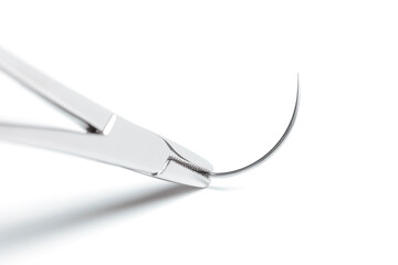Macro photo of artery forceps holding half circle cutting needle on white background. 