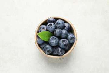 Tasty fresh blueberries in bowl on light table, top view