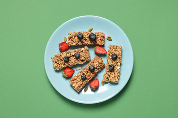 Tasty granola bars and berries on green background, top view