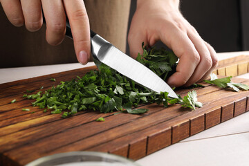 Woman cutting fresh parsley at white wooden table, closeup