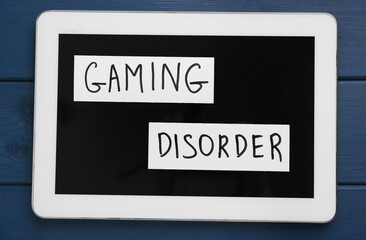Tablet with phrase Gaming Disorder on blue wooden table, top view. Addictive behavior