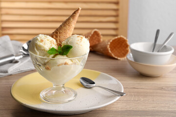 Delicious scoops of vanilla ice cream with wafer cone and mint in glass dessert bowl on wooden table