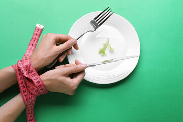 Diet concept. Woman holding cutlery in hands tied with measuring tape over plate with lettuce leaf...