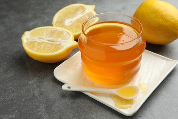 Sweet honey and fresh lemons on grey table, closeup. Space for text