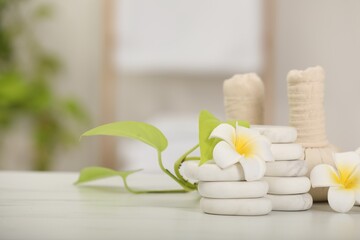 Spa composition. Herbal bags, stones, plumeria flowers and green leaves on white marble table, space for text