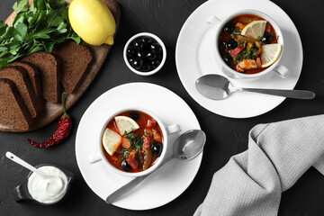 Meat solyanka soup with sausages, olives and vegetables served on dark grey textured table, flat lay
