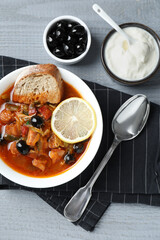 Meat solyanka soup with sausages, olives and vegetables served on grey wooden table, flat lay