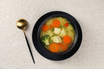 Tasty chicken soup with noodles and vegetables in bowl served on light textured table, top view