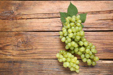 Delicious fresh green grapes and leaves on wooden table, flat lay. Space for text