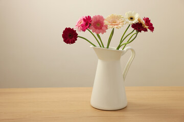 Jug with beautiful gerbera flowers on wooden table. Space for text